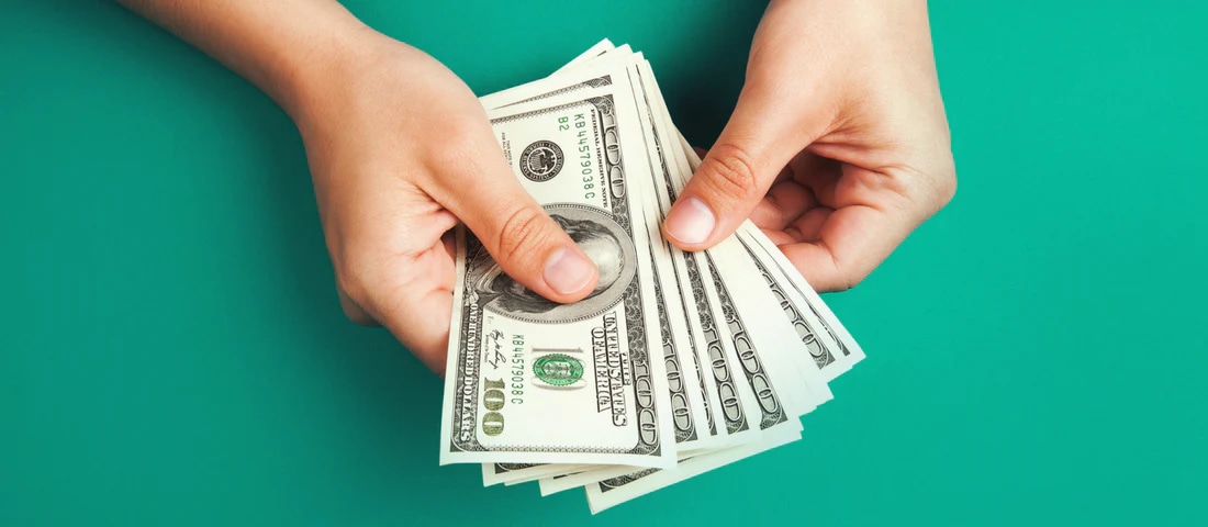 Hands holding a stack of US dollar bills against a green background.