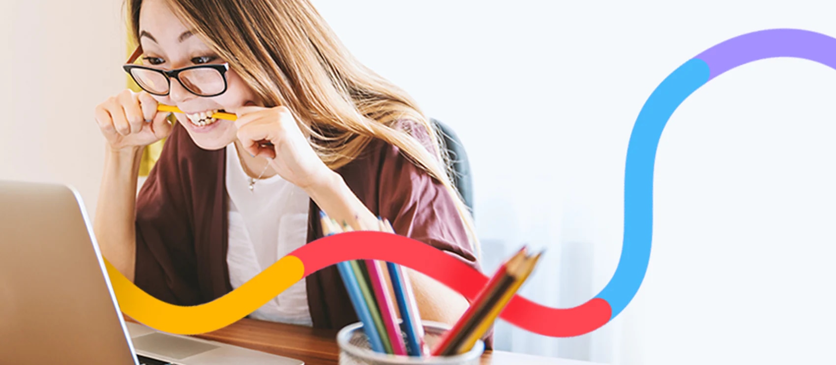 Woman biting pencil in frustration while working on a laptop, illustrating the benefits of outsourcing photo edits for productivity.