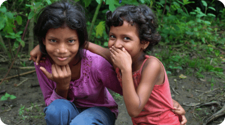 Two smiling girls in a rural setting, symbolizing Path's efforts in creating jobs and fostering professional skills in local communities.